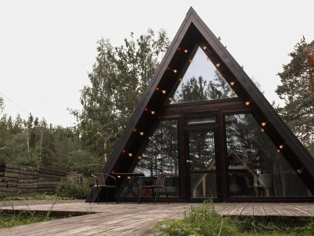 Малый A-frame в светлых тонах с гамаком-сеткой до 4 гостей, A-frame домики Forest Tale в Дегтярске: A-frame с гирляндой на фасаде