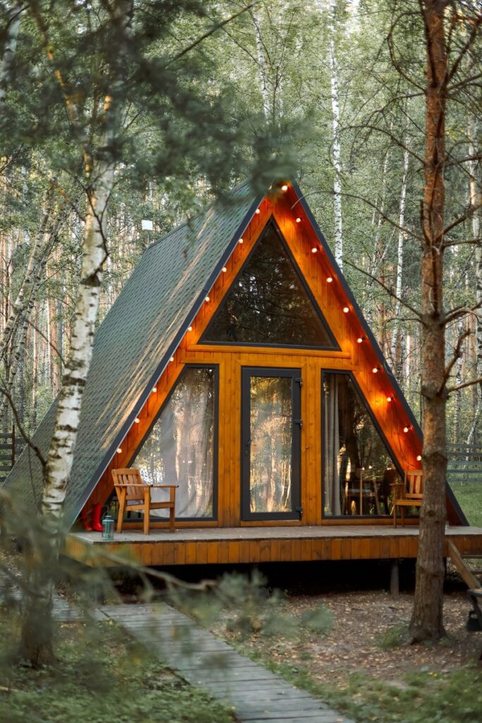 Маленький A-frame дом 36 м² с подвесным креслом, шесть одинаковых: фасад с гирляндой вечером