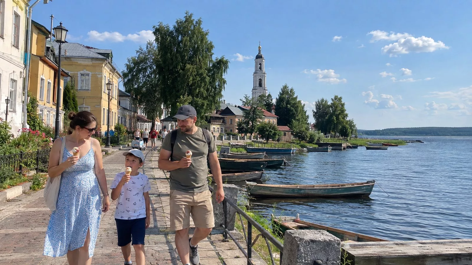 Семья с мороженым гуляет по набережной Осташкова у старых двухэтажных домов и колокольни, у берега деревянные лодки